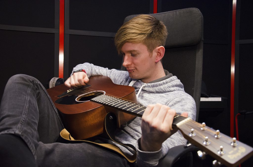 Musikproduzent Lukas Lach mit Gitarre in seinem Studio