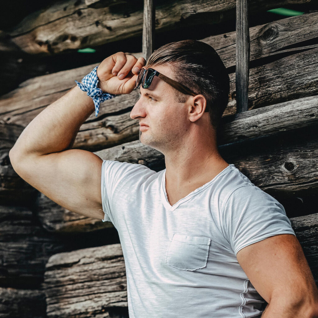 Florian Andreas, Holzhütte, brauner Hintergrund, Lederhose, Blick in die Ferne